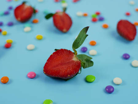sliced fresh strawberries and colorful sweet candy on blue background. concept