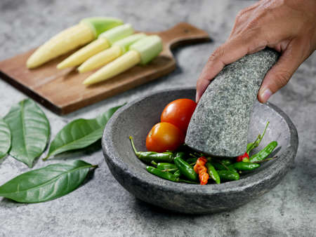 hands are grinding chilies and tomatoes with a mortar to make chili sauce. vegetarian food preparation concept.の写真素材
