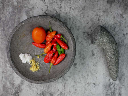top view of red chilies, tomatoes, and seasonings in a mortar ready to make chili sauce. cooking concept.の写真素材