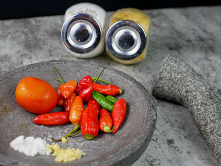 Red chilies, tomatoes, and seasonings in a mortar are ready to make chili sauce. cooking concept.の写真素材