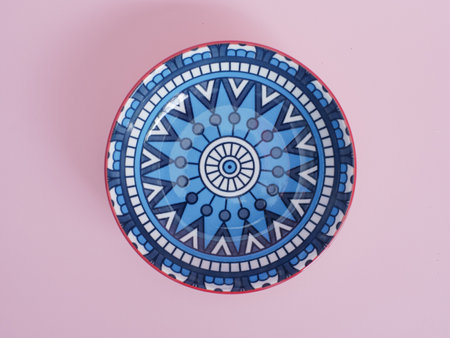 Colorful ceramic plate on pastel pink background, top view.