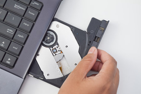 Close-up of human hand opening CD drive on laptop, minimal technology concept showing optical disc...