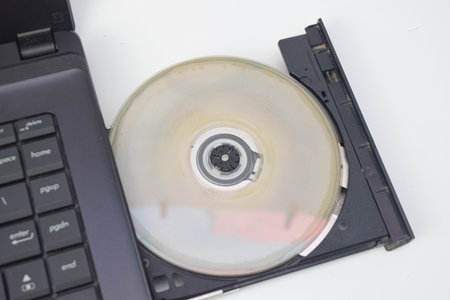 Laptop with optical drive containing a stained CD, realistic tech photo showing aging hardware and data storage device, suitable for maintenance, vintage, or technology conceptの写真素材