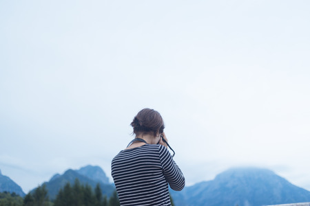 Girl in striped casual clothing with camera in front of mountains and sky