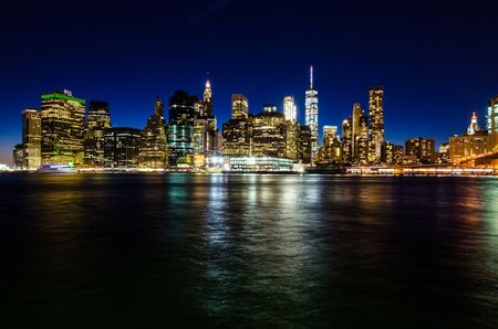 View of illuminated Manhattan skyline at twilight, with skyscraper lights reflected on the river. New York City, USAの写真素材