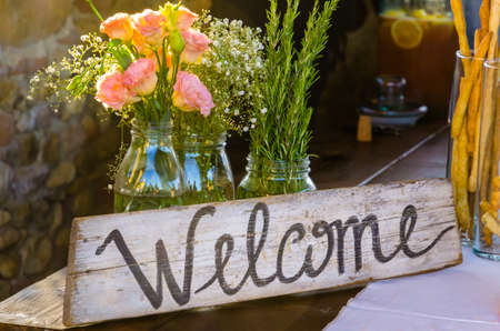 Welcome sign painted on wood next to a bunch of pink flowersの写真素材