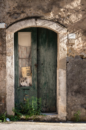 Old wooden door of an abandoned house with a for sale sign, Italyの写真素材