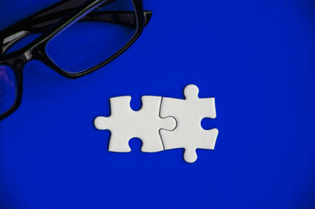 Top view of pieces of jigsaw puzzle with glasses on blue cover background. Copy space conceptの写真素材