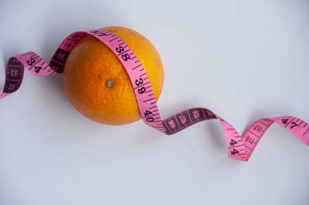 Measuring tape and orange on white background. Weight loss and fitness conceptの写真素材