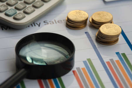 Analysis of data, chart and graphs with calculator, magnifying glass and gold coins background. Business finances and accounting conceptの写真素材