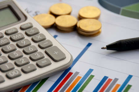Analysis of data, chart and graphs with calculator, pen and gold coins background. Business finances and accounting conceptの写真素材