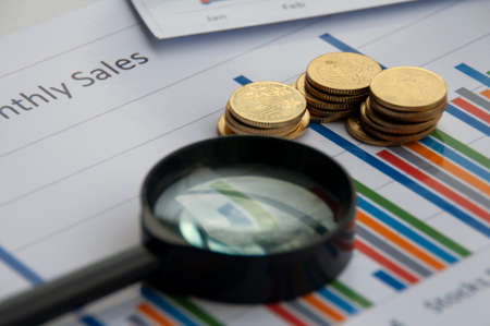 Analysis of data, chart and graphs with magnifying glass and gold coins background. Business...
