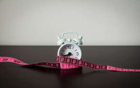 Straight view of white alarm clock wrapped with measuring tape background. Fitness concept.の写真素材