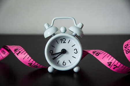 White alarm clock with measuring tape background. Fitness concept.の写真素材