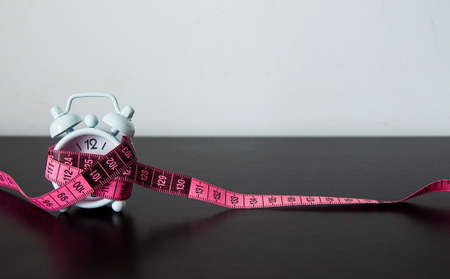 Side view of white alarm clock wrapped with measuring tape background. Fitness concept.の写真素材