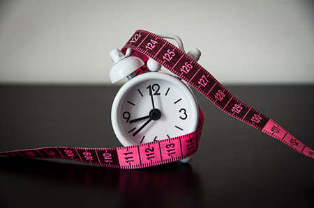 White alarm clock wrapped with measuring tape background. Fitness concept.の写真素材