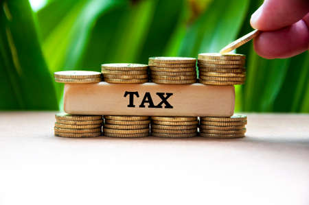 Tax text on wooden block with stack of gold coins on blurred background.の写真素材
