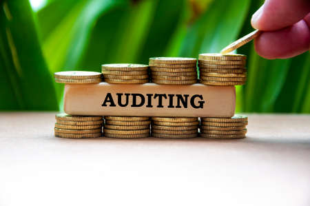 Auditing text on wooden block with stack of gold coins on blurred background.の写真素材