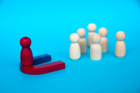 Hand holding magnet attracting wooden dolls on yellow background. Law of attraction concept.の写真素材