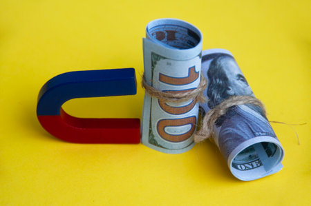 Hand holding magnet attracting wooden dolls on yellow background. Law of attraction concept.の写真素材