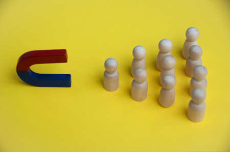 Hand holding magnet attracting wooden dolls on yellow background. Law of attraction concept.の写真素材
