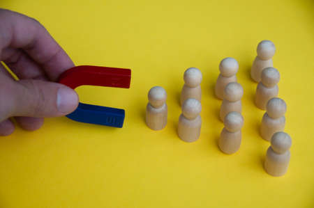 Hand holding magnet attracting wooden dolls on yellow background. Law of attraction concept.の写真素材