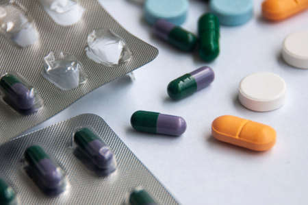 Assorted pharmaceutical medicine pills, tablets and capsules with blurred background over white...