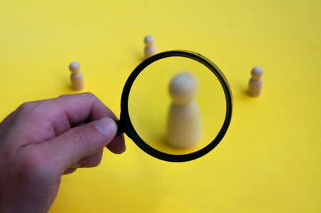 Hand holding magnifying glass focusing on wooden figure. Employment concept.の写真素材
