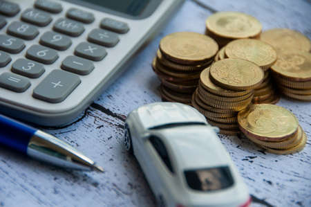 Gold coins, calculator, white car toy and pen on wooden background. Selective focus on coins. Finance and copy space conceptの写真素材
