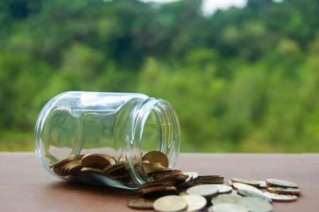 Gold coins on wooden table with blurred nature background. Copy space