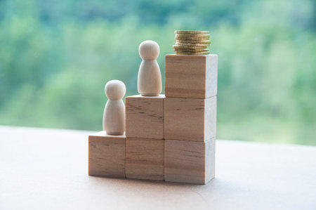 Wooden dolls and gold coins on top of stacking wooden blocks. Goal achieving concept and copy spaceの写真素材
