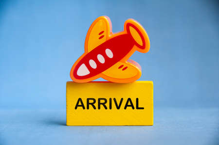 Arrival text on yellow wooden block with toy plane on top. Travelling conceptの写真素材