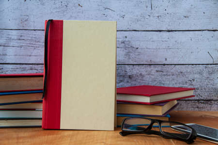 Blank book cover with stack of books, glasses and smart phone on wooden table. Copy spaceの写真素材