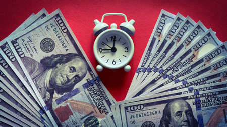 Top view of white alarm clock and bank notes on red background. Copy spaceの写真素材