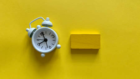 Alarm clock on yellow background with small wooden. Copy space