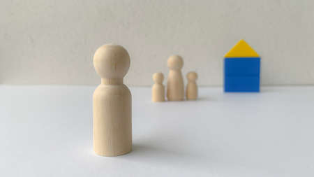 Wooden doll family stands in front of house model. Family concept