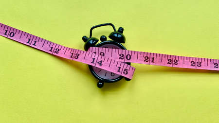 Measuring tap on alarm clock and yellow paper. Weight loss and fitness concept