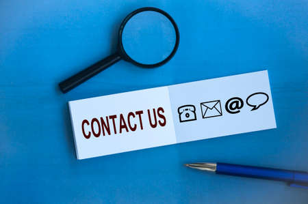 Contact us text with icons on notepad on blue background. Business concept