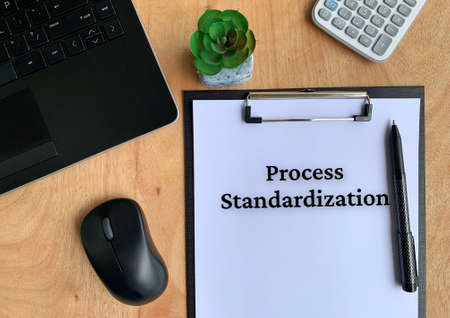 Process standardization text on a paper with pen, plant, mouse, laptop, calculator and brown table background.の写真素材