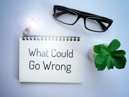 Top view of what could go wrong text on notebook with shining bulb, glasses and plant background.の写真素材