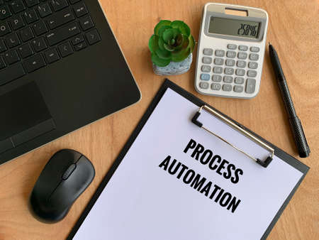 Process automation text written on paper with laptop, pen, calculator, mouse and brown table background.の写真素材