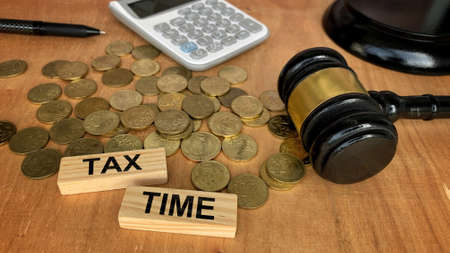 Tax time text on wooden blocks with coins, gavel, calculator background.の写真素材