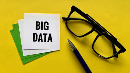 Top view of white sticky note with Big Data text. With minutes glasses and pen background.の写真素材