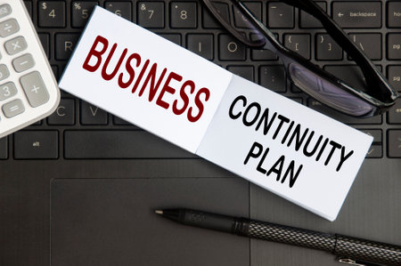 Business continuity plan text on notepad with glasses, pen and laptop background. Business continuity conceptの写真素材