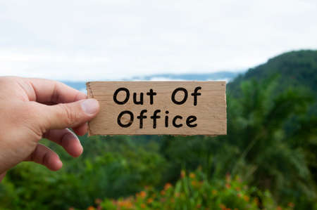 Hand holding wooden banner with text - Out of office.の写真素材