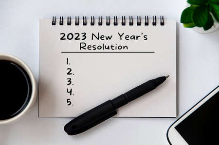 2023 New Year's Resolutions text on note pad with pen, smart phone, plant and coffee.の写真素材