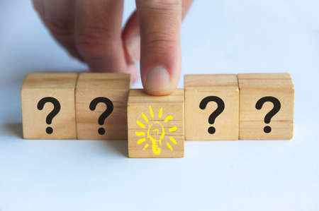 Hand pointing at wooden cube block with light bulb surrounded by questions marks. Solution and idea conceptの写真素材
