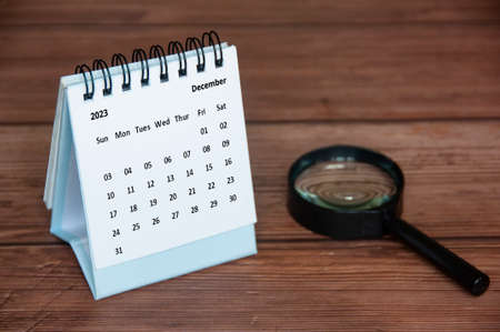 December 2023 white desk calendar with magnifying glass on wooden table. Calendar concept and copy spaceの写真素材