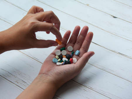 Female hand picking one pill isolated on wooden background. Copy space and Medical conceptの写真素材