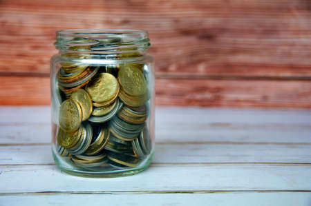 Coins in a jar on wooden table with customizable space for text or ideas. Copy space and business conceptの写真素材